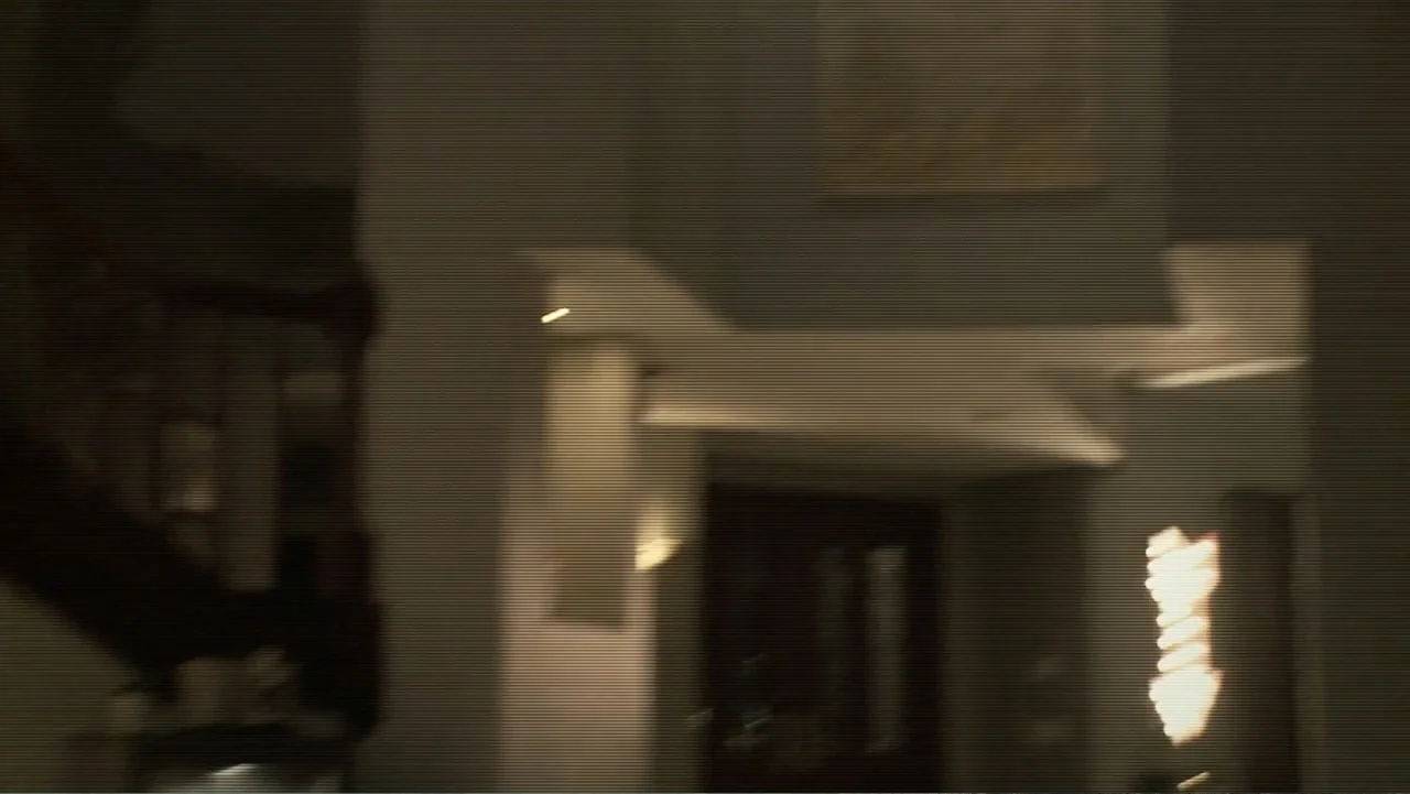 Paranormal Activity: The Ghost Dimension (2015) movie still: establishing — A dark house foyer with a staircase and dimly lit wall sconces. The…