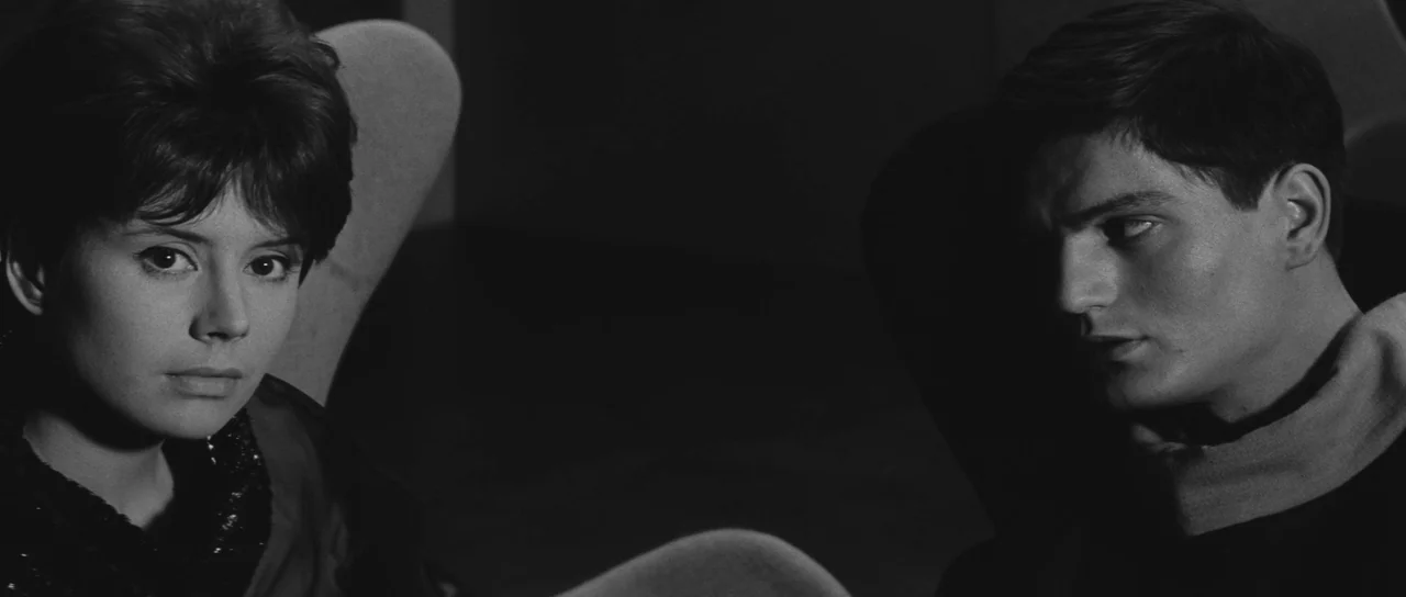 Ikarie XB 1 (1963) movie still: medium — Two individuals sit in a dark room with curved high-backed chairs. The man watches the woman as she faces…