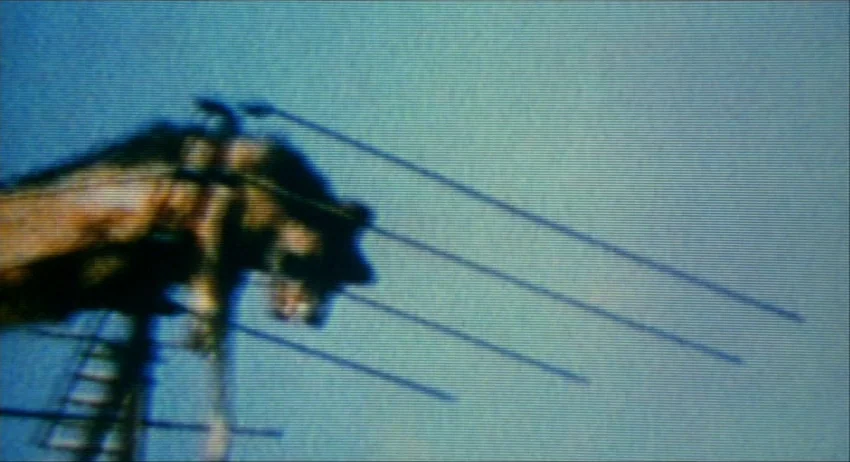 Gummo (1997) movie still: closeup — A dark, weathered gargoyle statue sits atop a building against a clear sky. A multi-pronged television antenna…