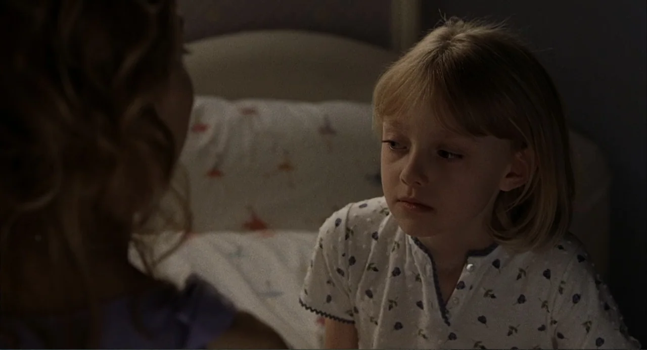 Uptown Girls (2003) movie still: medium — A dimly lit bedroom features a child sitting on a bed with patterned linens. The child looks toward an…