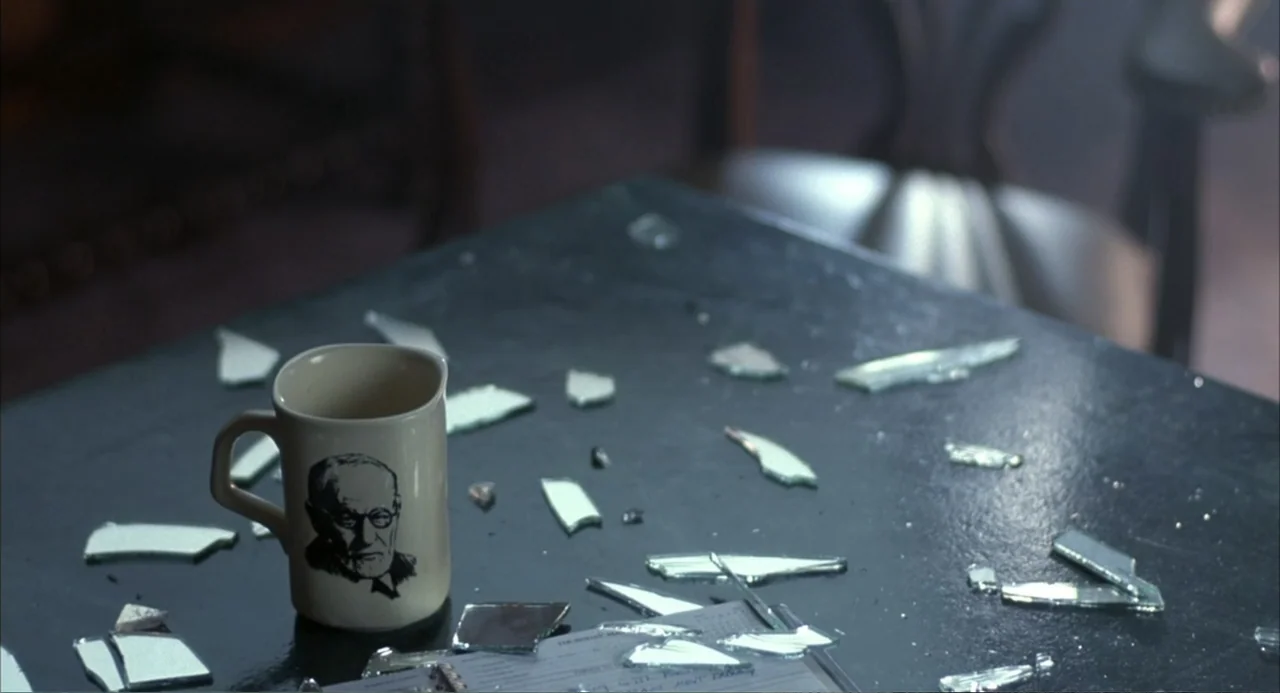 Poltergeist III (1988) movie still: closeup — A dark office desk is covered with scattered glass shards and a ceramic mug. A personal organizer lies…