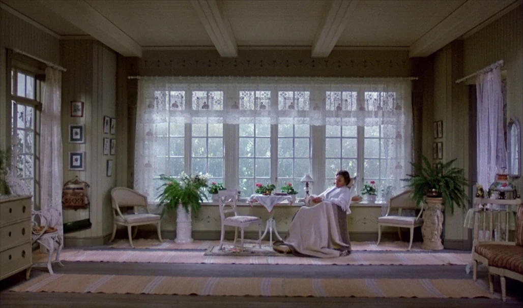 Fanny and Alexander (1982) movie still: wide — A sunlit room features pale green wooden walls and a large, wide window arrangement. A woman sits in…