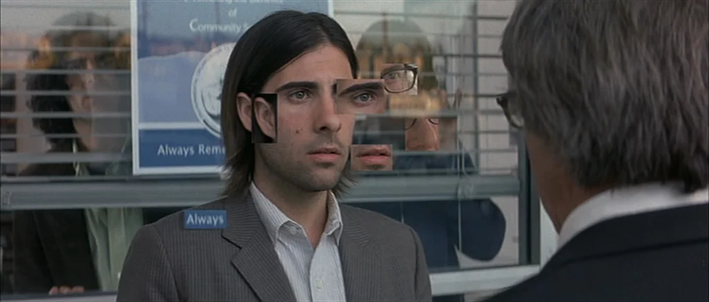 I Heart Huckabees (2004) movie still: medium — A man in a grey suit stands before a window with reflected text signage. He gazes forward while…