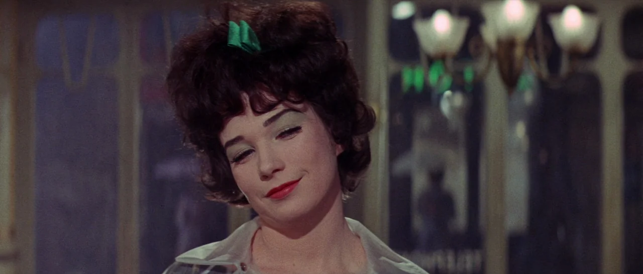 Irma La Douce (1963) movie still: closeup — A woman stands in a warmly lit, slightly blurred interior space at night. She has her eyes closed and…