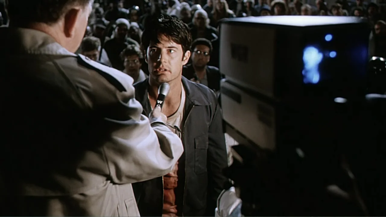 Against the Wall (1994) movie still: medium — A crowded press event with a man speaking directly into a held microphone. He stands in the foreground…