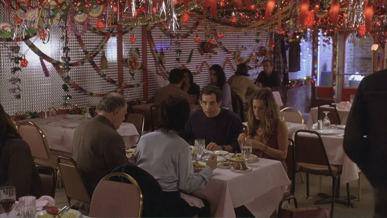 Along Came Polly (2004) movie still: medium — A restaurant dining room decorated with hanging red ribbons and holiday lights. Four people sit at a…