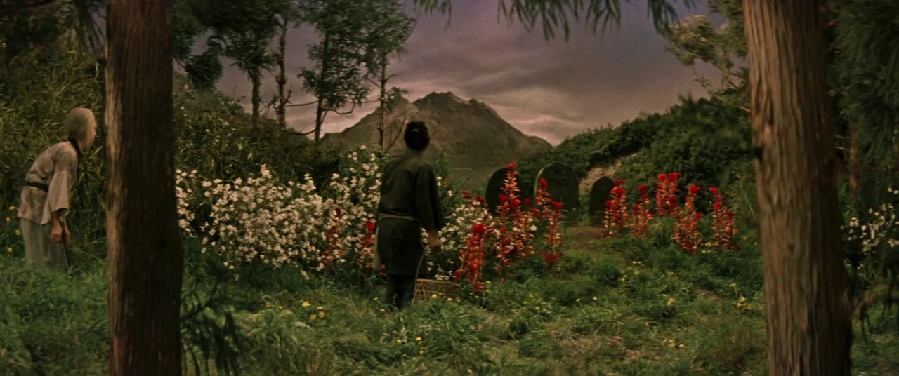 Ballad Of Narayama (1958) movie still: wide — A lush meadow filled with white and red flowers sits before rolling distant mountains. Two people…