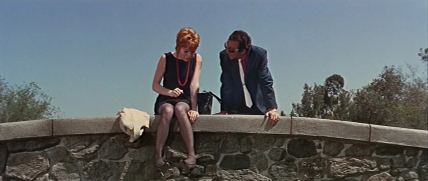 Sweet Charity (1969) movie still: fullbody — Two people sit together atop a rugged stone wall under a clear blue sky. The man in a suit looks down…