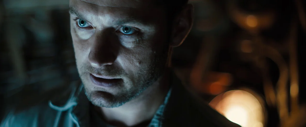 Black Sea (2014) movie still: closeup — A dimly lit interior space with mechanical equipment in the background. A man stares intently while…