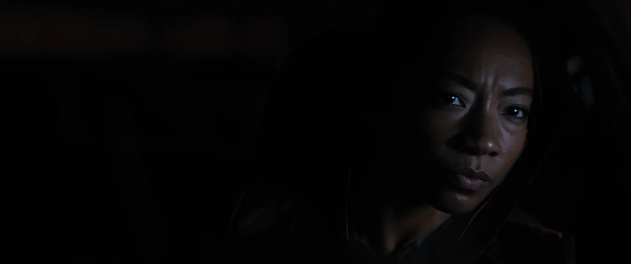 Upgrade (2018) movie still: closeup — A woman sits inside a car in a darkened environment at night. She gazes slightly off-camera toward the side of…