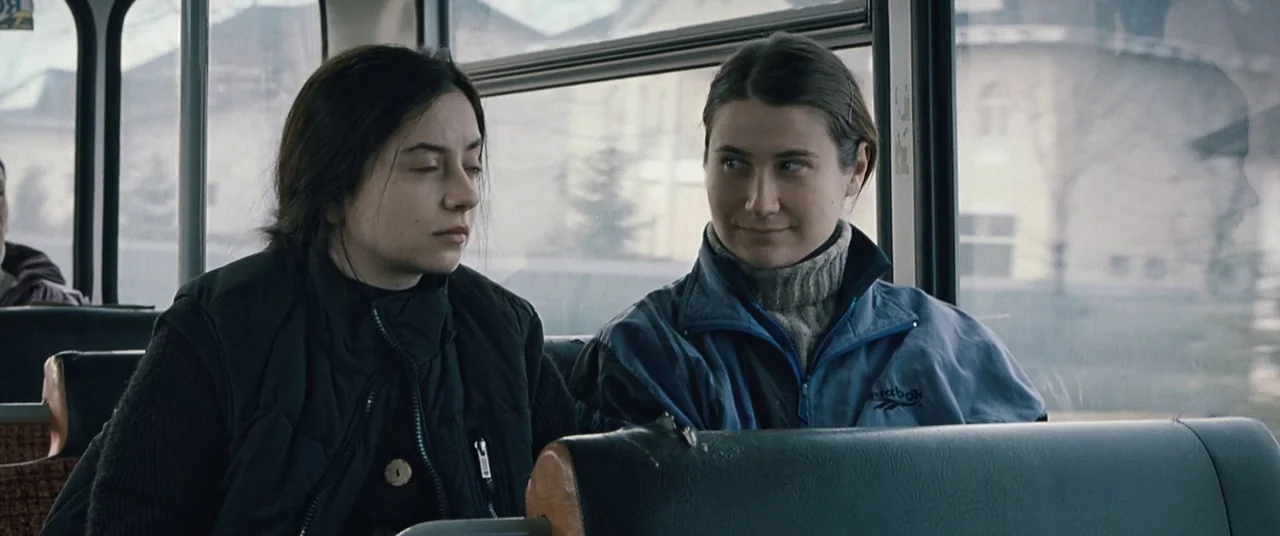 Beyond the Hills (2012) movie still: medium — A bus interior with rows of seats and windows looking out onto a street. Two women are sitting…