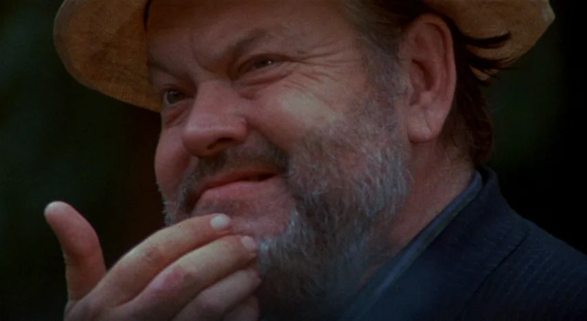 A Safe Place (1971) movie still: closeup — A man stands outdoors wearing a straw hat. He rests his fingers against his bearded chin.