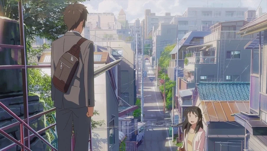 Your Name (2016) movie still: wide — An urban residential area features a steep descending street lined with multi-story buildings. A man in a suit…