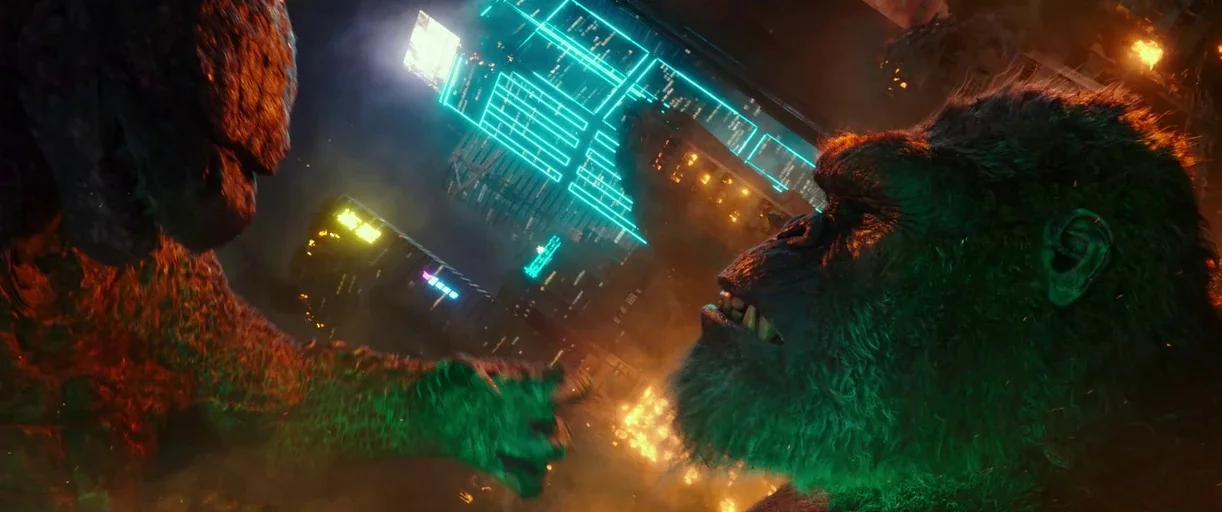 Godzilla Vs. Kong (2021) movie still: medium — A destroyed city skyline filled with glowing blue neon signage and burning debris. Two massive kaiju…
