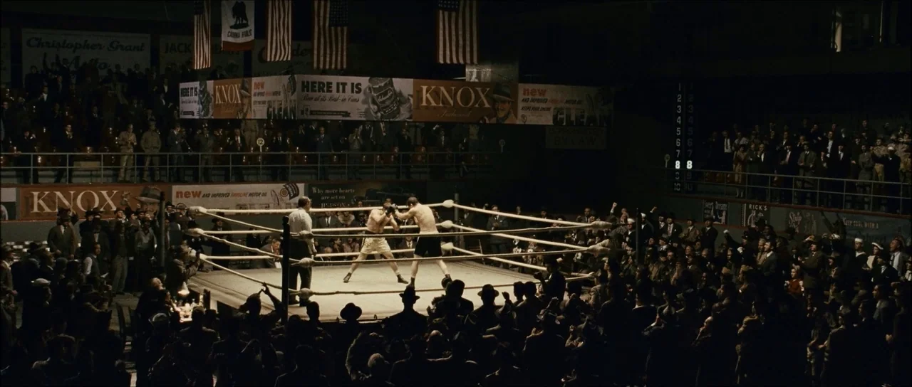 The Black Dahlia (2006) movie still: wide — A high-angle view of a dimly lit arena filled with spectators surrounding a fight ring. Two boxers…