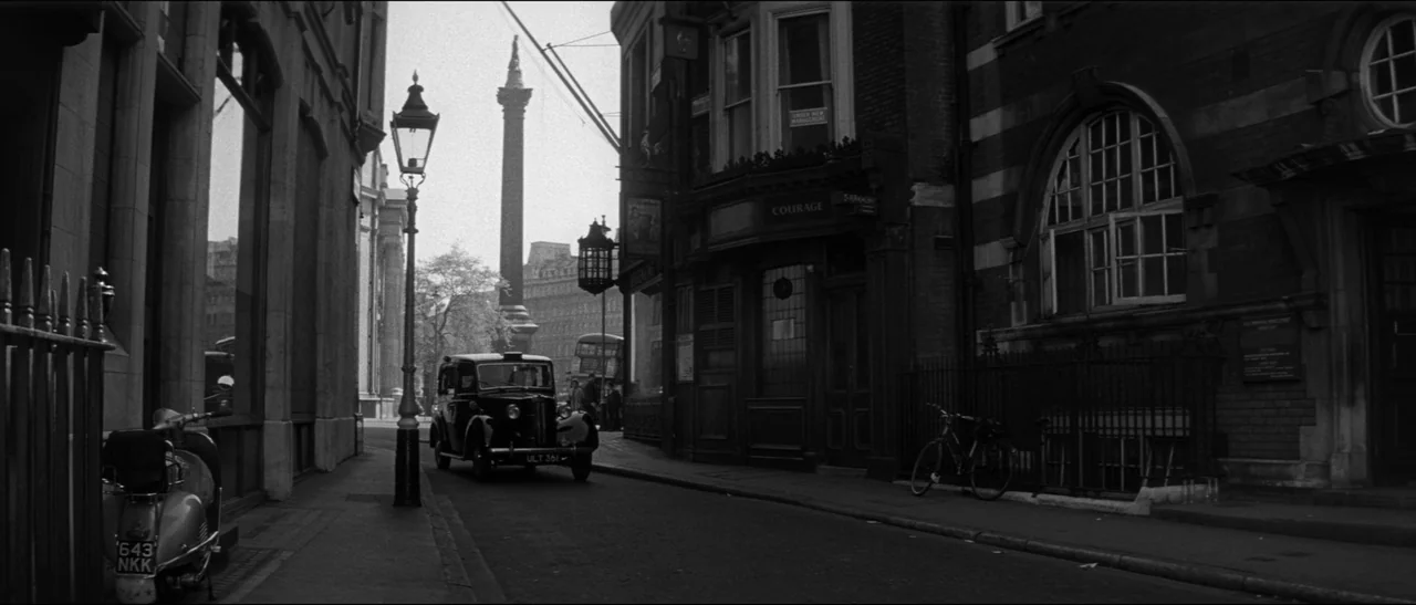 Bunny Lake Is Missing (1965) movie still: wide — A London street corner features a dark brick building with an arched window. A vintage black…