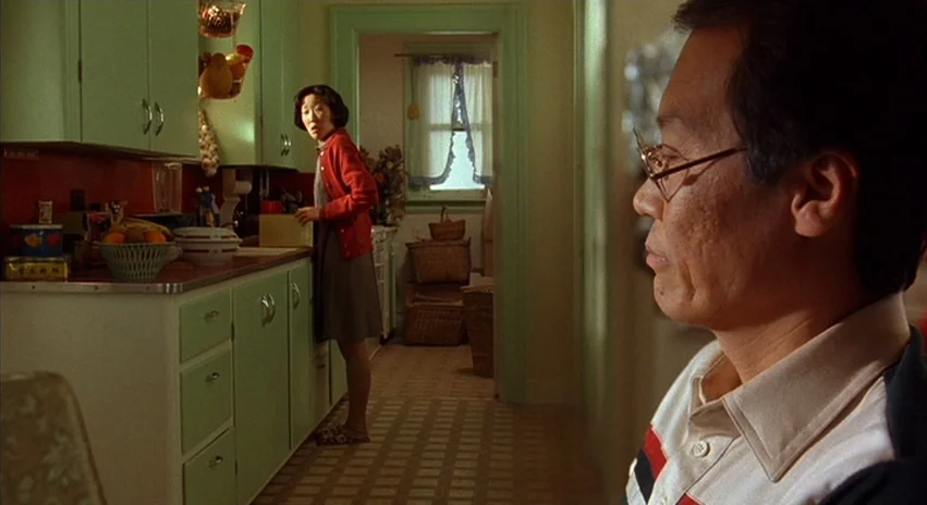 Double Happiness (1994) movie still: medium — A 1950s style room has pastel green cabinets and patterned linoleum flooring. A man looks toward a…