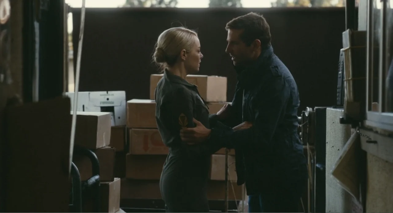 Aloha (2015) movie still: medium — A cluttered loading area is filled with stacks of brown cardboard packing boxes. A man grabs a woman by the arms…