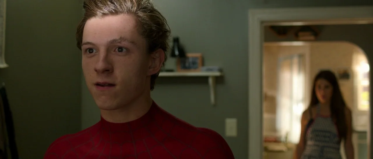 Spider Man: Homecoming (2017) movie still: medium — A dimly lit room with muted green walls and a wall shelf featuring framed items. A young man in…