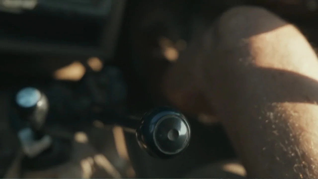 Bloody Trophy (2025) movie still: closeup — An interior of a vehicle focused on the gear shift lever. A hand is out of focus gripping the shifter.