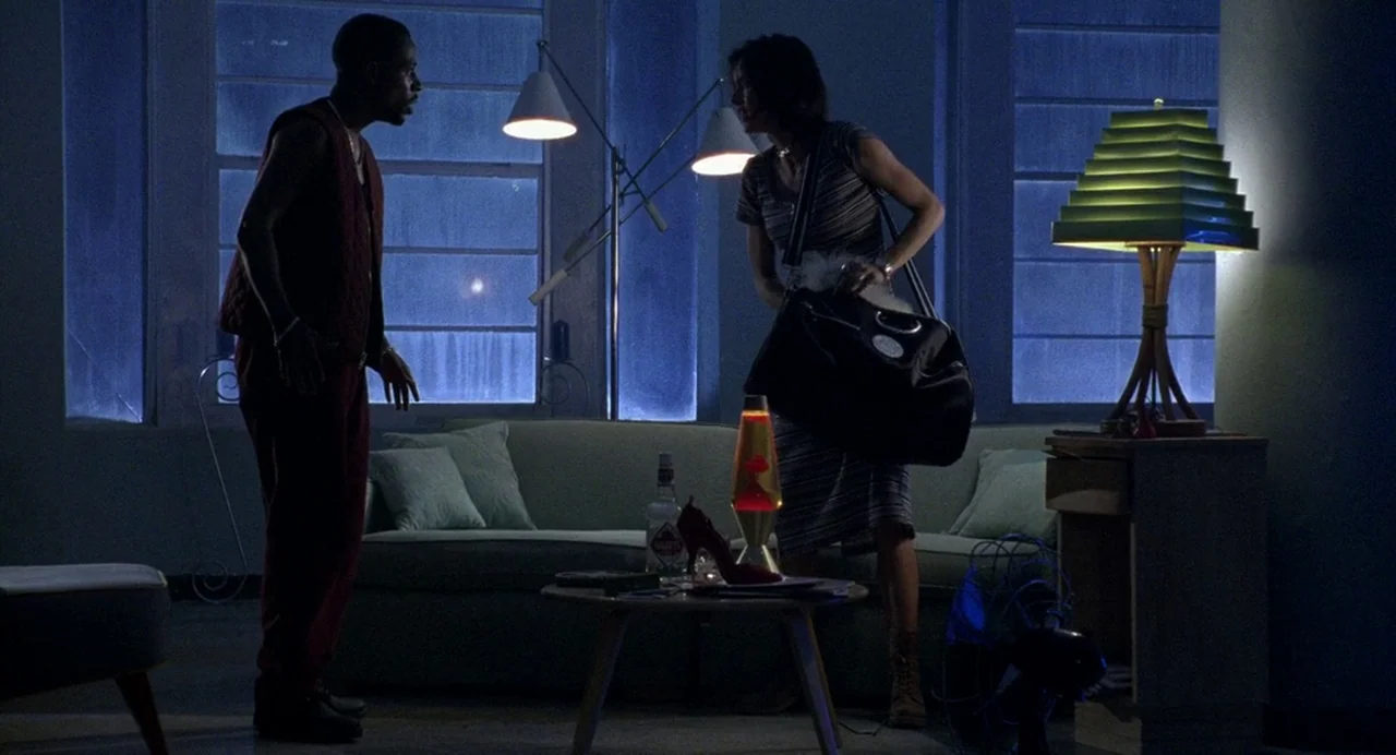 Bad Boys (1995) movie still: medium — A dimly lit room with large windows features a sofa, a coffee table, and lamps. A woman packs a black bag…