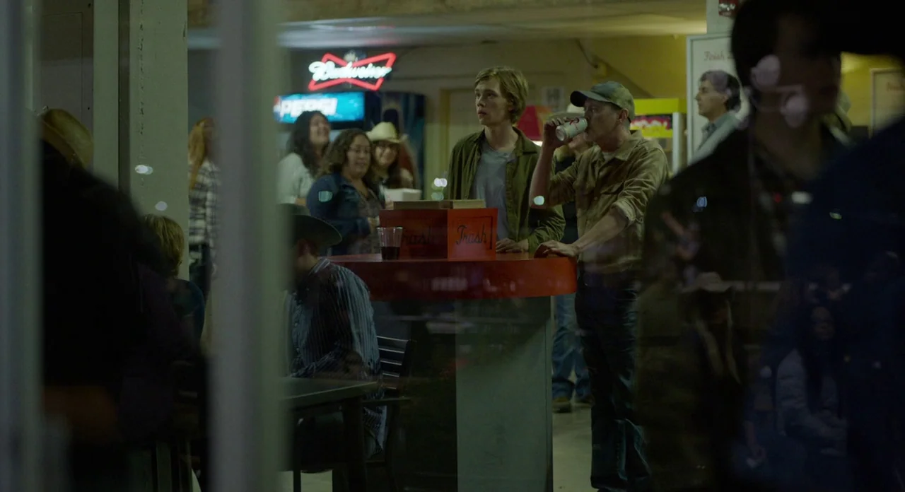 Lean on Pete (2017) movie still: medium — A dimly lit indoor concession area features a central red stand with trash bins. A man drinks from a can…