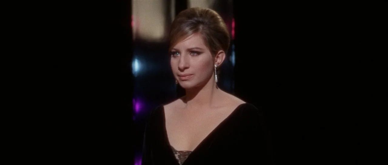 Funny Girl (1968) movie still: closeup — A dark stage with reflective surfaces behind a woman dressed in black velvet. The subject stands center…