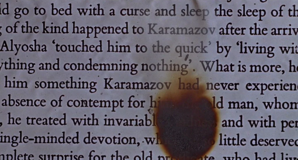 Fahrenheit 451 (1966) movie still: closeup — A close-up view of a page from a printed book featuring black text. A distinct, circular burn hole with…