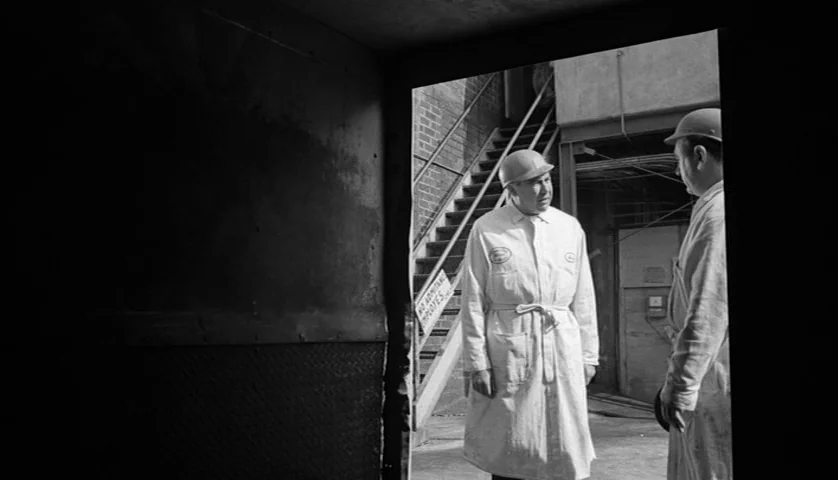Seconds (1966) movie still: medium — An industrial exterior features a brick staircase leading upward beside a metal doorway. Two men in white work…