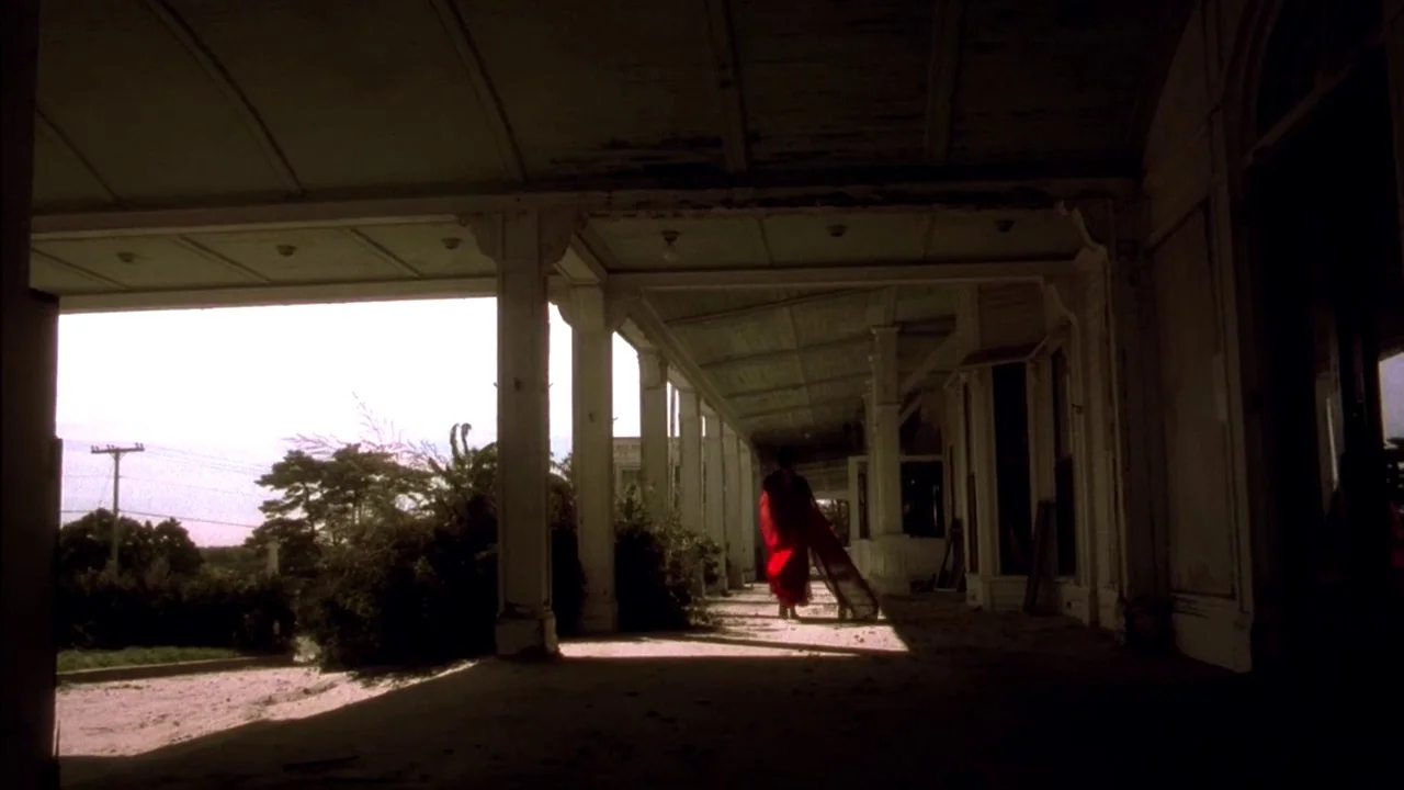 In Dreams (1999) movie still: wide — A long, white, wooden covered veranda stretches alongside a building with evenly spaced columns. A solitary…