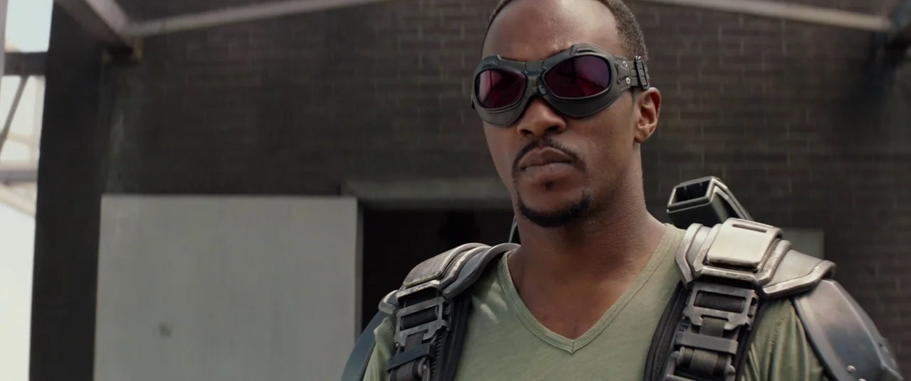 Captain America: The Winter Soldier (2014) movie still: medium — A man stands before a dark brick wall of an industrial building exterior. The…