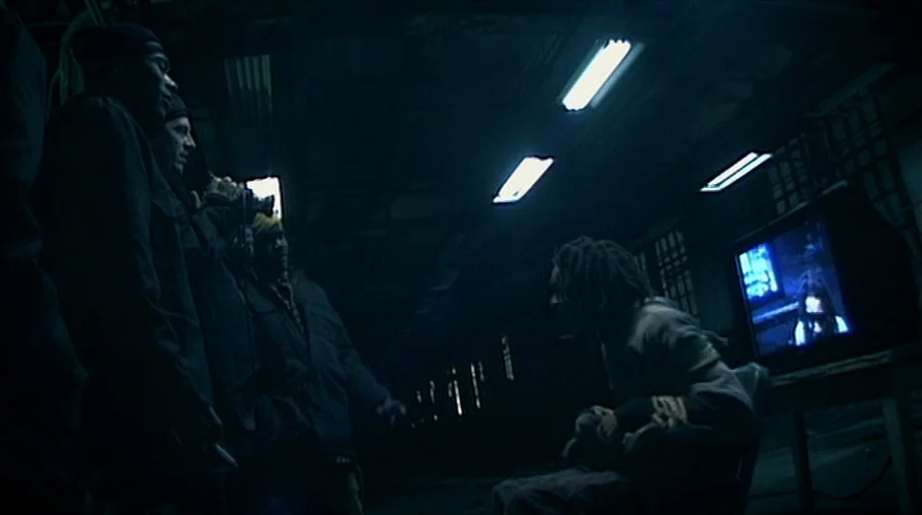 Bamboozled (2000) movie still: medium — A dark, cavernous industrial space with overhead fluorescent lighting and visible structural pillars. A…