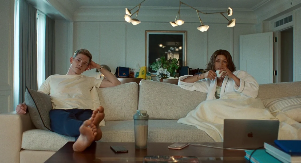 Challengers (2024) movie still: medium — A spacious hotel suite features a beige sofa and a modern sputnik-style chandelier. A man and a woman…