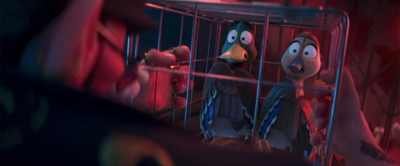 Migration (2023) movie still: medium — A dimly lit interior space features two ducks trapped inside a metal cage. A person's hand with gold rings…