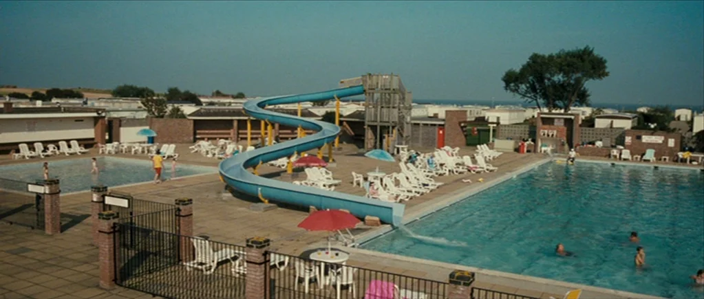 The Scouting Book for Boys (2009) movie still: wide — A recreational facility features a large swimming pool and a prominent blue water slide.…