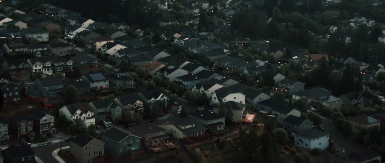 Night of the Missing (2023) movie still: establishing — A dense suburban residential area featuring numerous multi-story houses nestled among green…