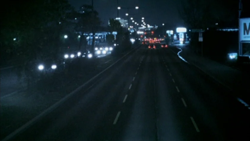 71 Fragments of a Chronology of Chance (1994) movie still: establishing — A multi-lane highway stretches into the distance under the dim glow of…