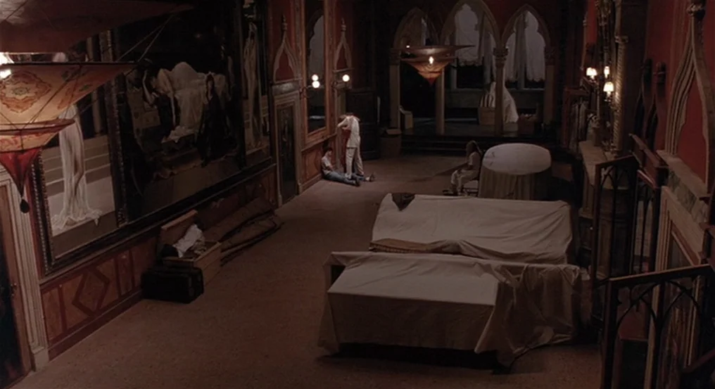 The Comfort of Strangers (1990) movie still: wide — A spacious, ornate room features high ceilings, red walls, and large paintings in frames. Three…