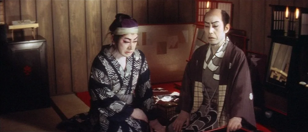 An Actor’s Revenge (1963) movie still: medium — Two individuals in traditional Japanese attire sit on red tatami mats inside a room. Wooden paneled…