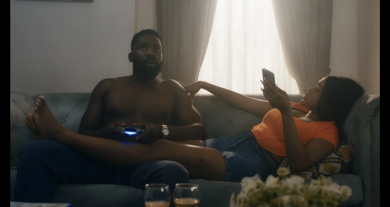 Love In A Pandemic (2023) movie still: medium — A light blue tufted couch is positioned in front of a bright window. A man playing a video game sits…