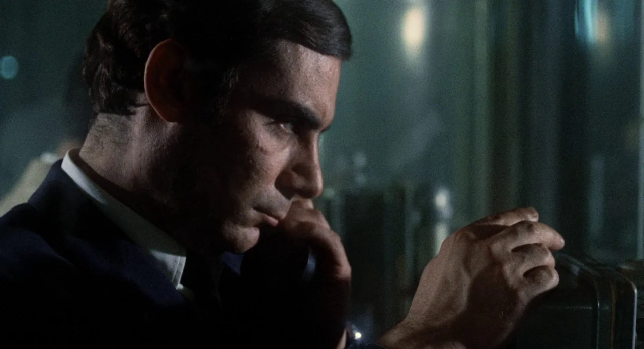 Investigation of a Citizen Above Suspicion (1970) movie still: closeup — A man stands in a dark space lit by dim, cool-toned light. He speaks into a…