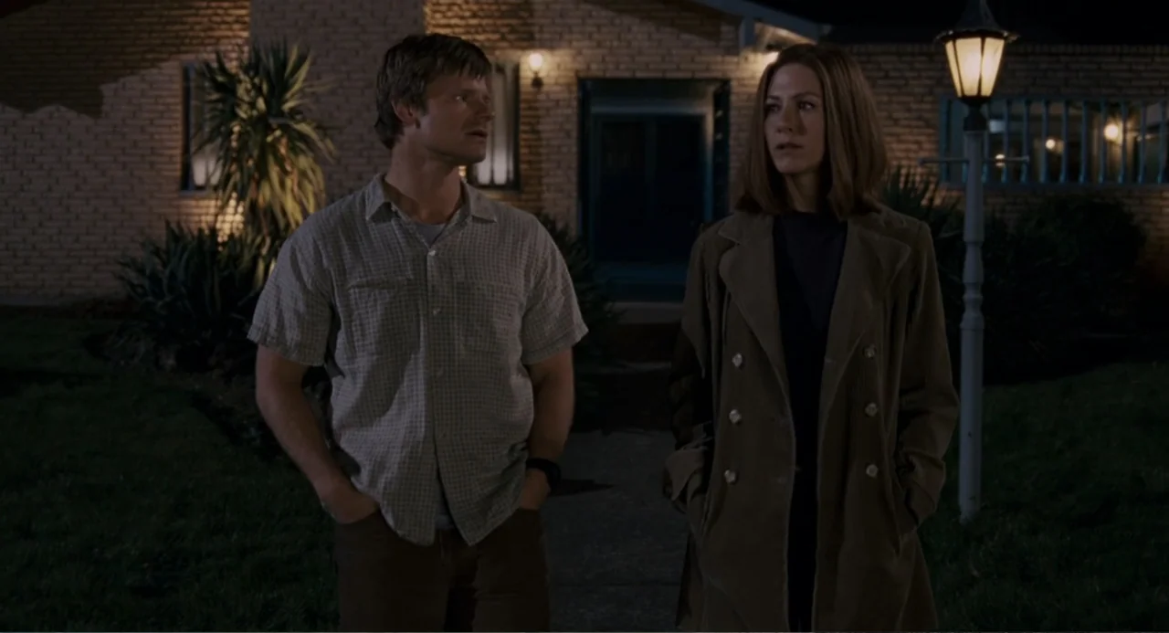 Management (2009) movie still: medium — A dark residential front yard features a brick-sided house in the background at night. A man and a woman…