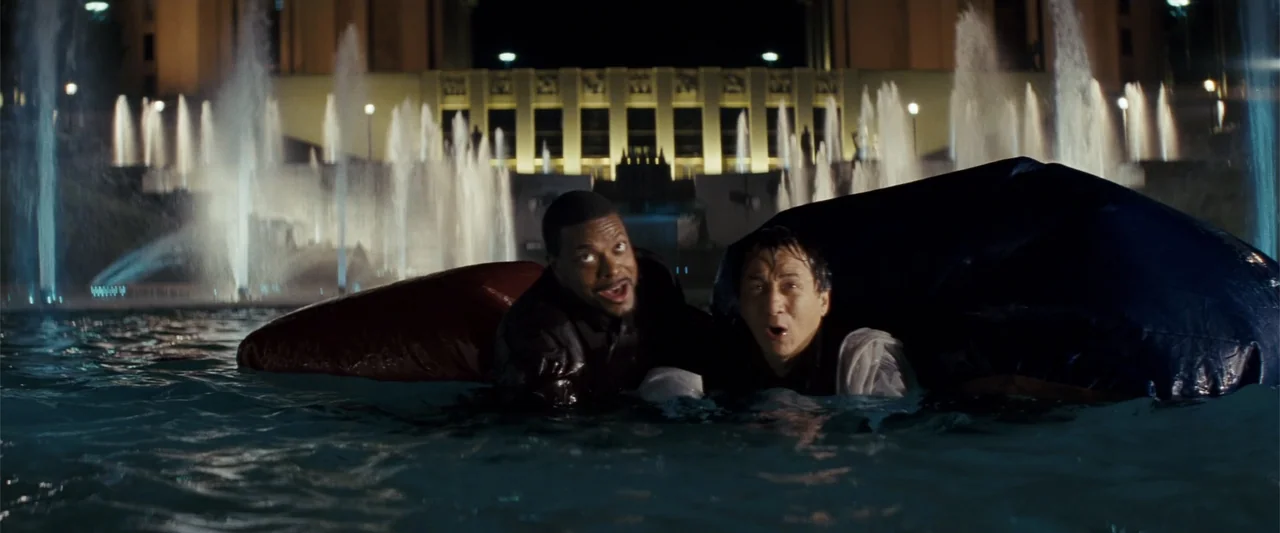 Rush Hour 3 (2007) movie still: medium — Two men stand in a large outdoor fountain at night with illuminated water jets. The subjects are partially…