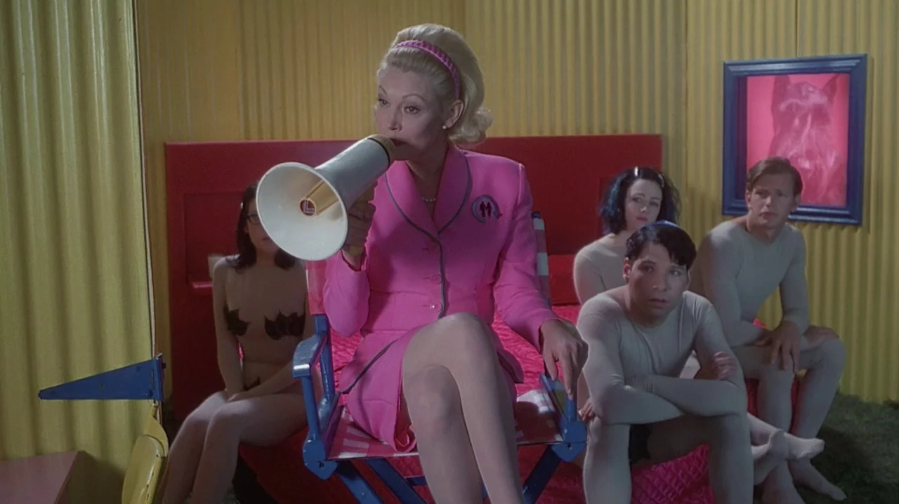 But I’m A Cheerleader (1999) movie still: medium — A room with yellow corrugated metal walls and a bright red bed frame. Five people in stylized…