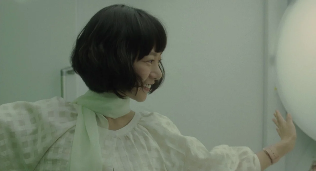 Air Doll (2009) movie still: medium — A woman stands in a bright room with pale green walls and minimal furniture. She reaches toward a large…