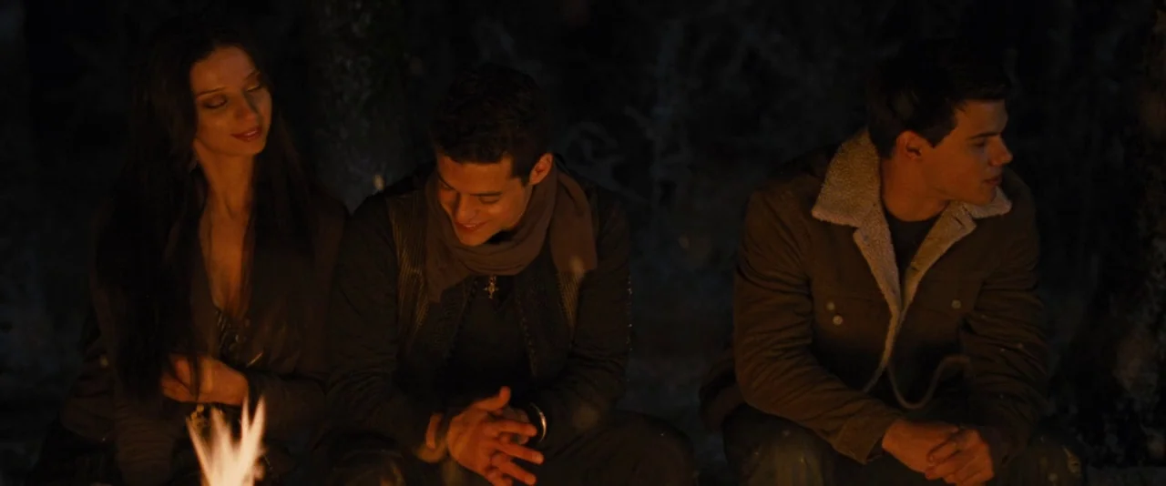The Twilight Saga: Breaking Dawn – Part 2 (2012) movie still: medium — A group of three people sit on the ground around a campfire at night. The…
