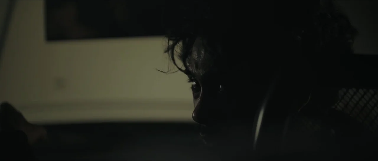 Innocent Vengeance (2023) movie still: closeup — A dimly lit room at night with a person sitting in the shadows. The person holds a telephone…