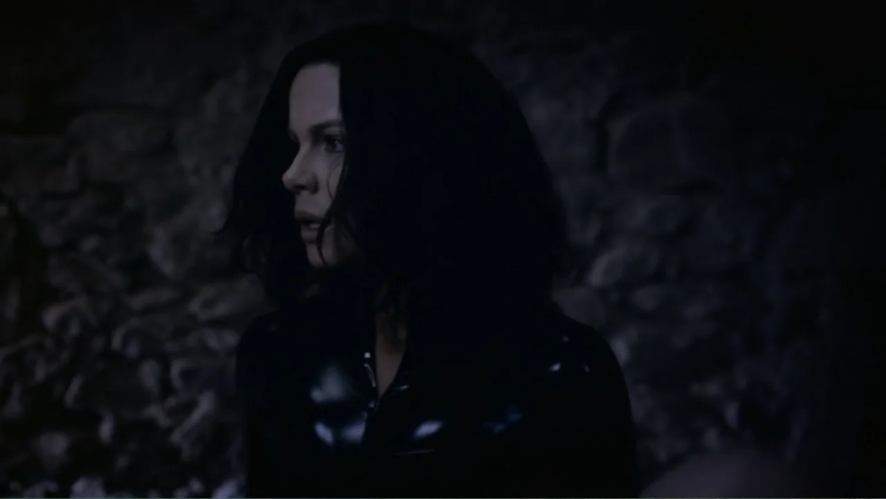 Underworld: Blood Wars (2016) movie still: medium — A dark, dimly lit stone chamber with rugged, textured walls serves as the backdrop. A woman with…