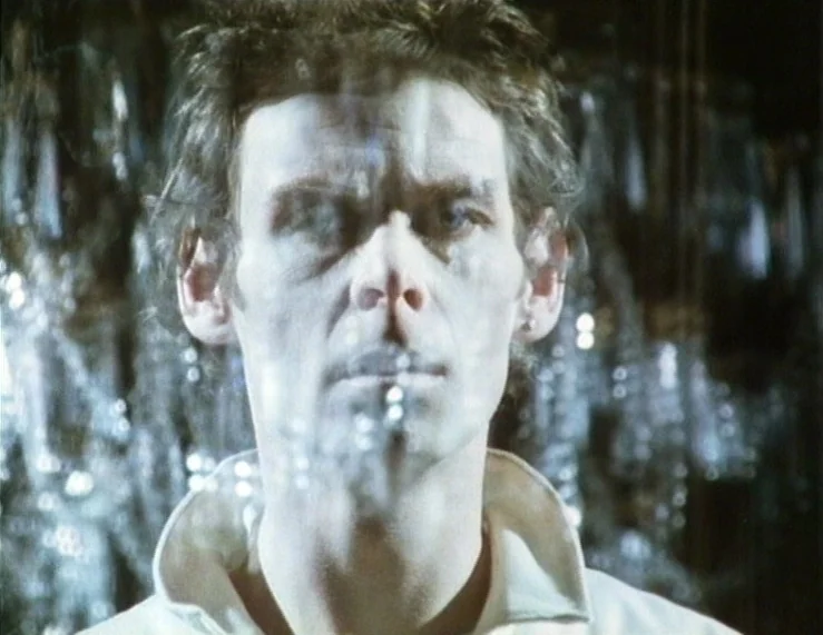 The Tempest (1979) movie still: closeup — A man's face is seen through a semi-transparent layer of bubbles or glass. The man looks directly into the…