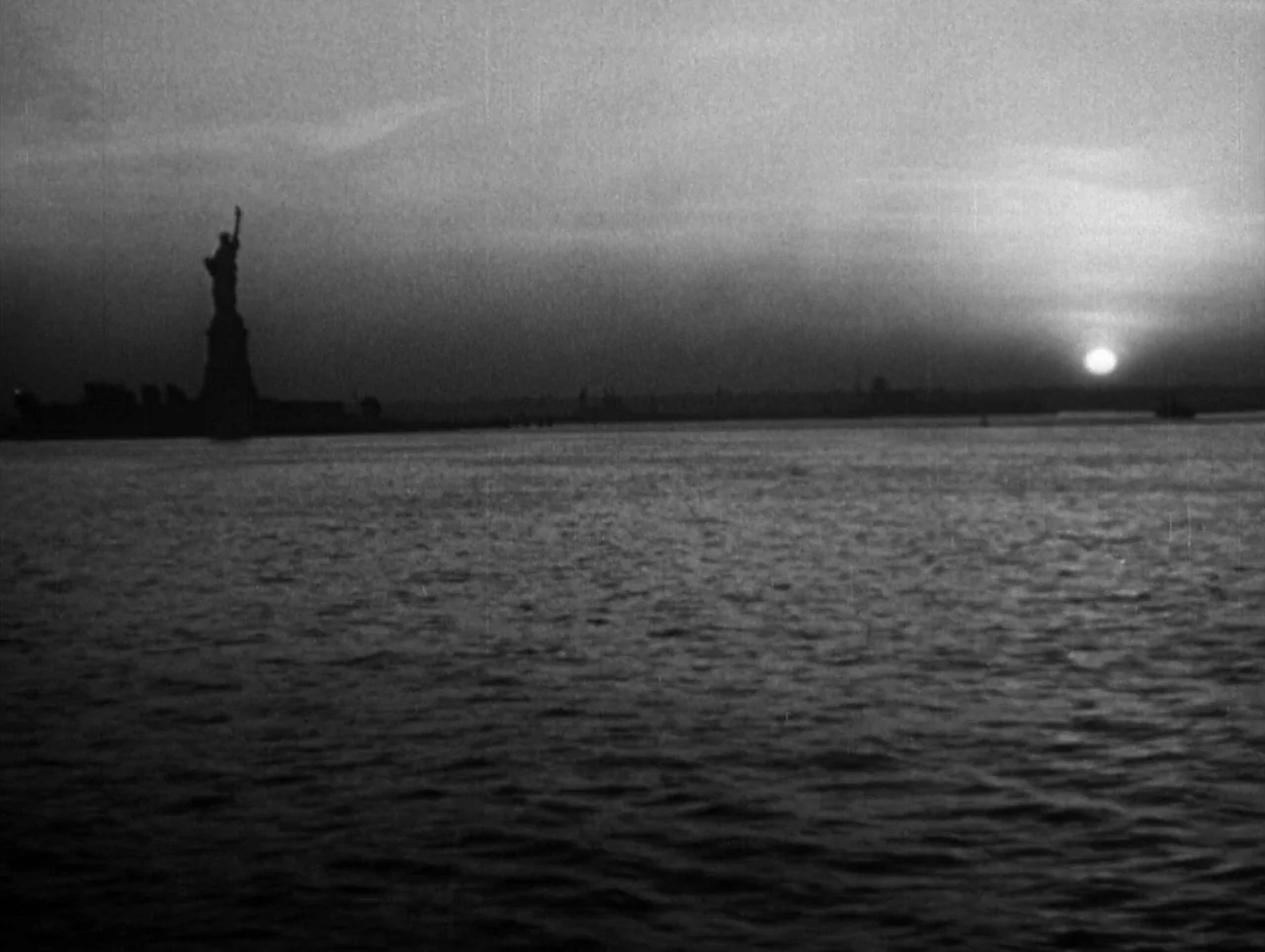 The Naked City (1948) movie still: establishing — A view of the Statue of Liberty silhouetted against a setting sun over harbor water. Rippled water…